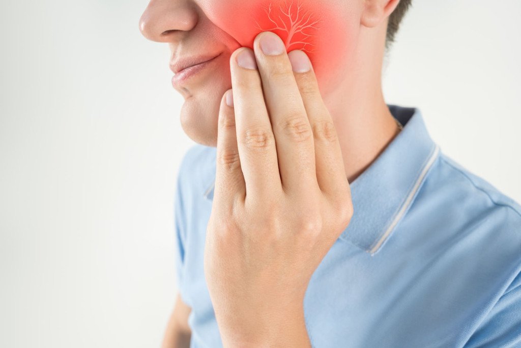 Personne tenant sa joue avec une zone rouge indiquant une douleur ou une inflammation dentaire, possiblement une douleur liée à une infection ou une carie.