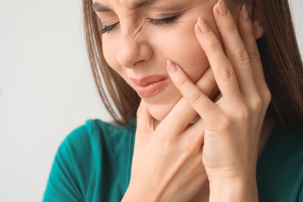 Femme exprimant de la douleur et tenant sa joue, suggérant qu'elle pourrait souffrir d'une douleur dentaire ou d'une infection des gencives.