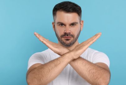 Un homme fait un signe de croix avec ses bras, représentant les choses interdites après une greffe de cheveux.