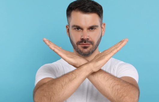 Un homme fait un signe de croix avec ses bras, représentant les choses interdites après une greffe de cheveux.