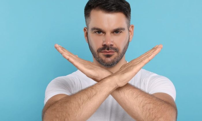 Un homme fait un signe de croix avec ses bras, représentant les choses interdites après une greffe de cheveux.