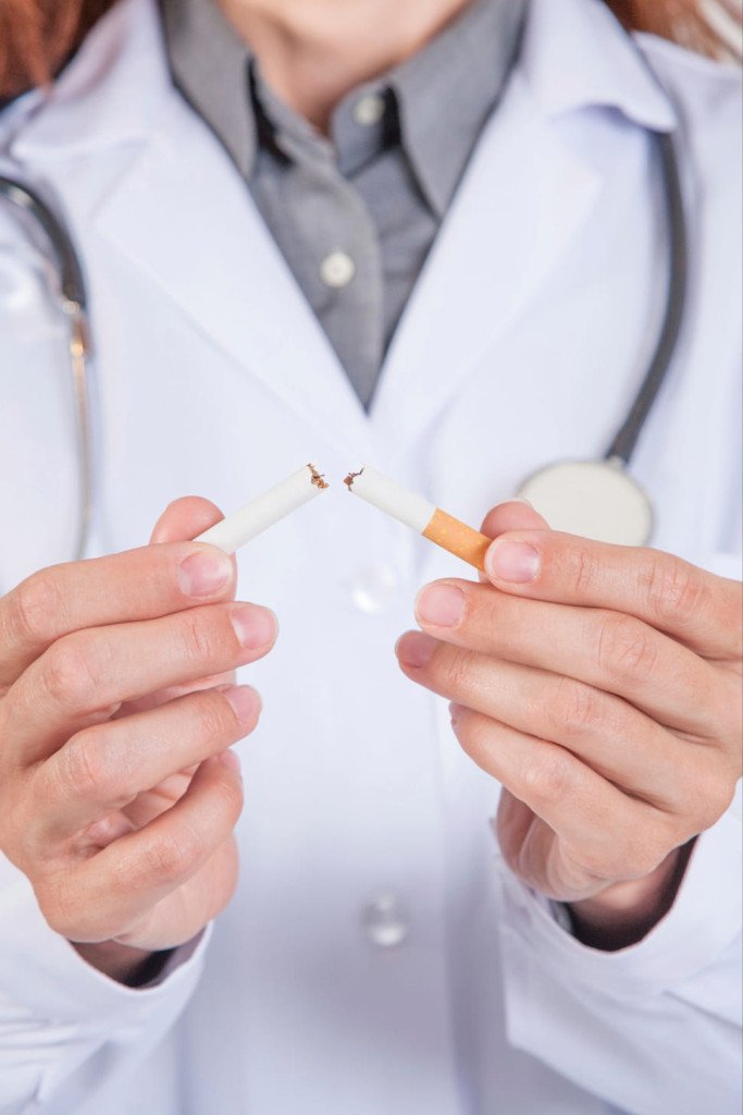 Un médecin en blouse blanche tenant une cigarette cassée en deux.