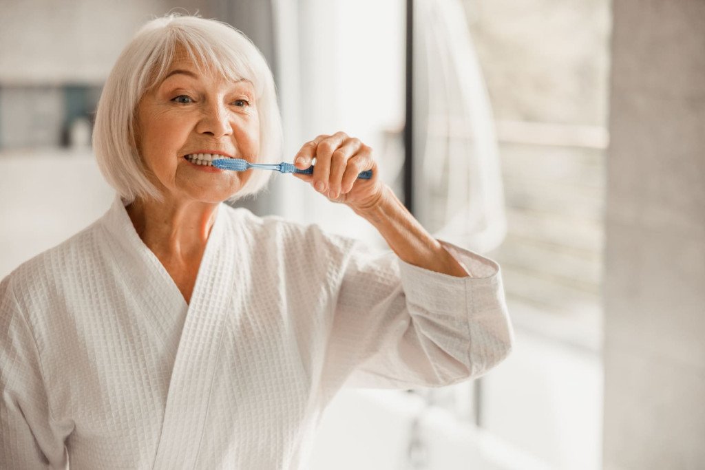Une femme âgée brosse ses dents, illustrant l'importance de l'hygiène bucco-dentaire avec l'âge.