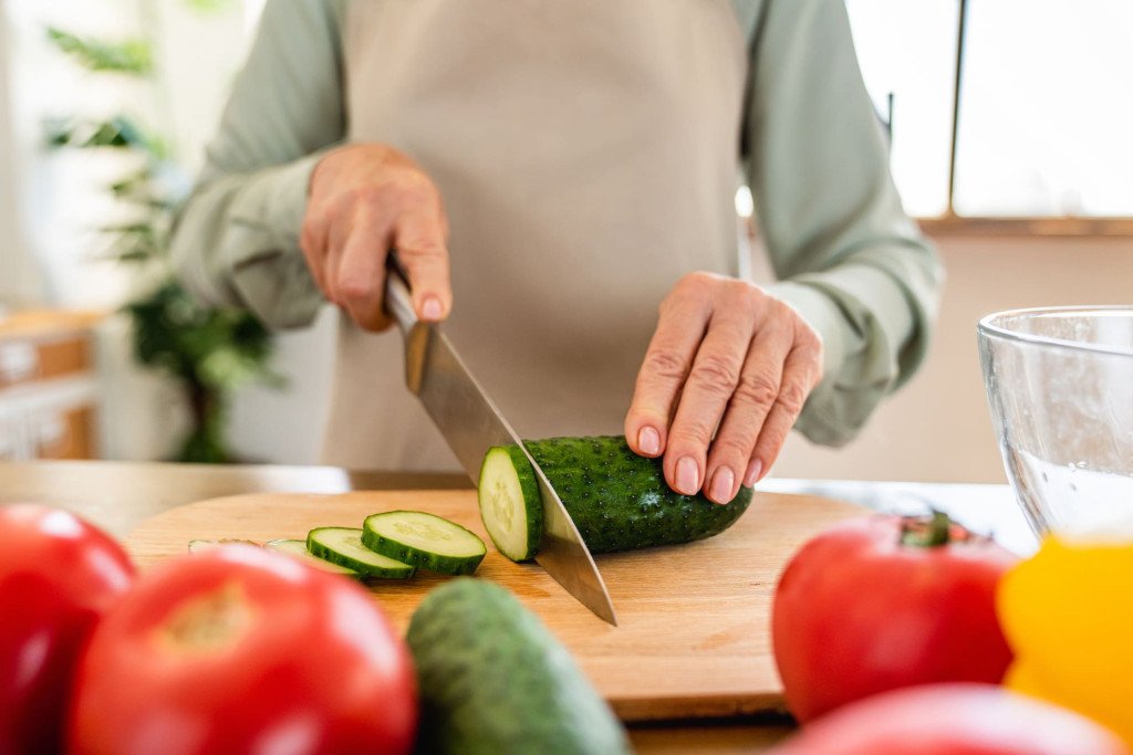 Une personne âgée coupe un concombre frais, illustrant l'importance d'une alimentation saine pour prévenir les problèmes dentaires liés à l'âge.