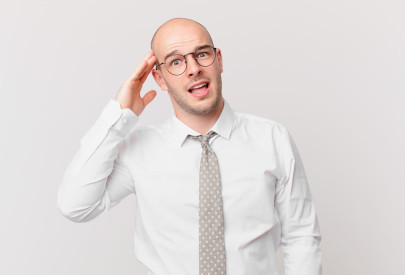 Homme chauve confus ajustant ses lunettes, représentant les préoccupations autour des risques de greffe de cheveux.