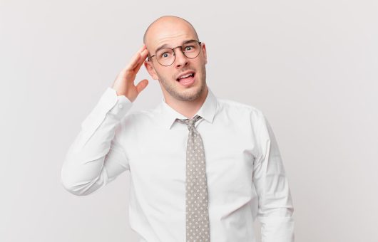 Homme chauve confus ajustant ses lunettes, représentant les préoccupations autour des risques de greffe de cheveux.