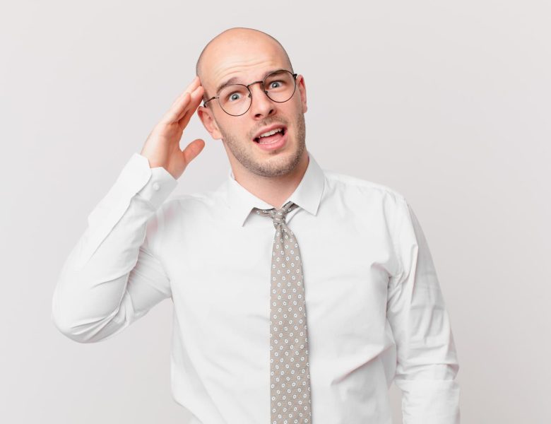 Homme chauve confus ajustant ses lunettes, représentant les préoccupations autour des risques de greffe de cheveux.