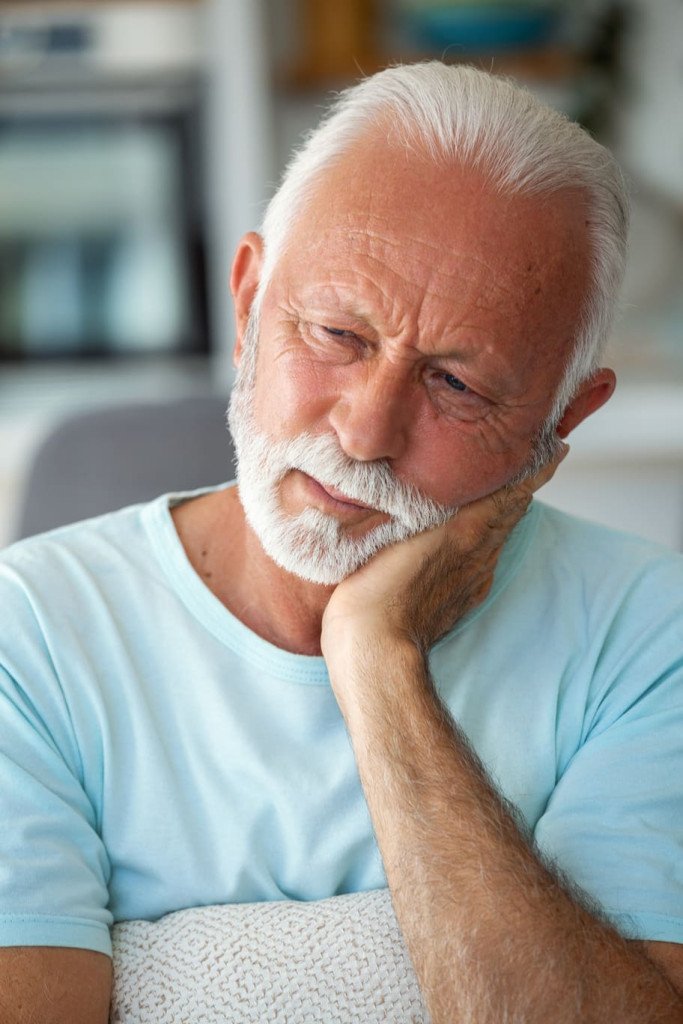 Un homme âgé se tenant la mâchoire avec une expression de douleur.